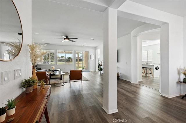 interior space featuring baseboards, arched walkways, ceiling fan, and wood finished floors