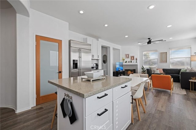 kitchen featuring recessed lighting, built in refrigerator, a fireplace, white cabinetry, and dark wood finished floors