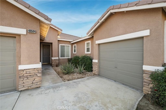 exterior space featuring an attached garage, stone siding, concrete driveway, a tiled roof, and stucco siding