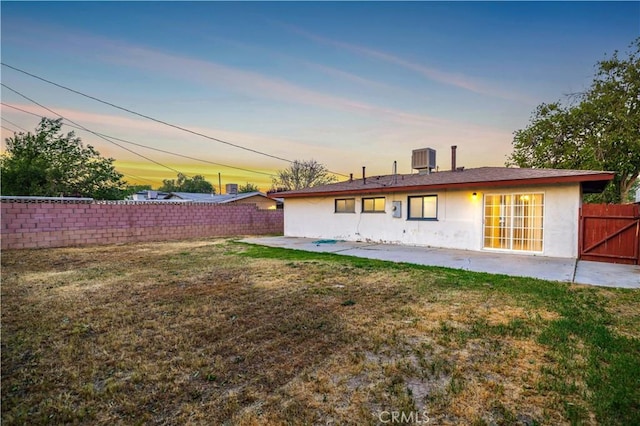 back house at dusk featuring a patio, a lawn, and central AC