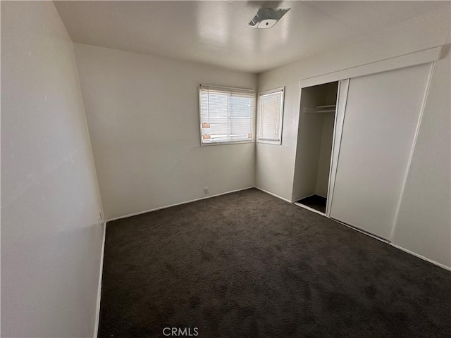 unfurnished bedroom with dark colored carpet and a closet