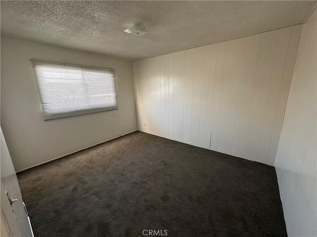 empty room with wood walls, a textured ceiling, and dark carpet