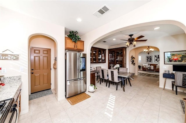 kitchen with light tile patterned flooring, ceiling fan with notable chandelier, light stone countertops, and stainless steel appliances