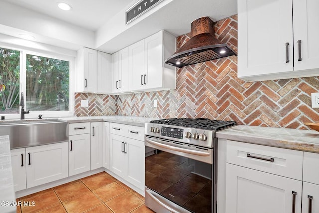 kitchen with stainless steel gas stove, wall chimney exhaust hood, white cabinets, tasteful backsplash, and light stone counters