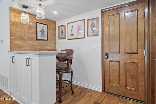 bar featuring light stone countertops, pendant lighting, white cabinets, and light hardwood / wood-style flooring