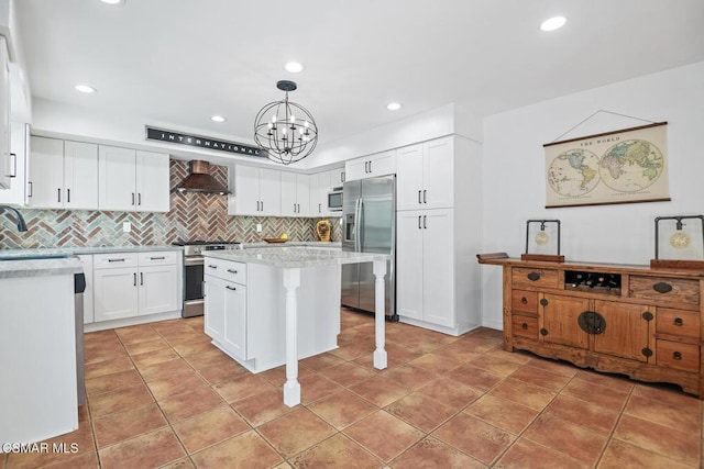 kitchen with pendant lighting, wall chimney exhaust hood, white cabinets, a kitchen island, and stainless steel appliances