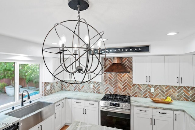 kitchen with pendant lighting, stainless steel gas range, white cabinetry, wall chimney range hood, and sink