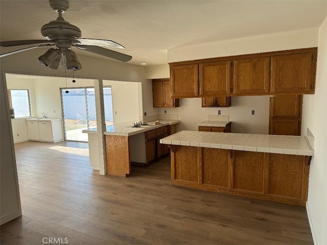 kitchen featuring sink, kitchen peninsula, dark wood-type flooring, ceiling fan, and tile countertops