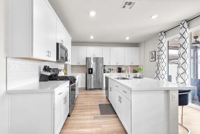 kitchen with sink, a kitchen island with sink, white cabinetry, stainless steel appliances, and a kitchen breakfast bar