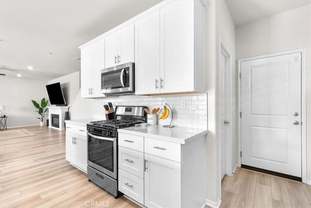 kitchen featuring stainless steel appliances, light hardwood / wood-style floors, decorative backsplash, and white cabinets