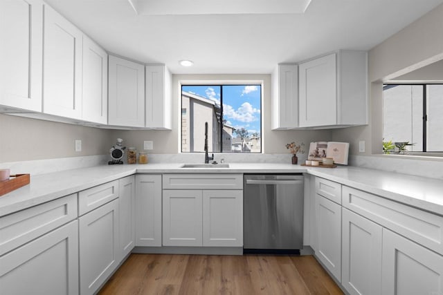 kitchen with light wood finished floors, stainless steel dishwasher, a sink, and white cabinetry