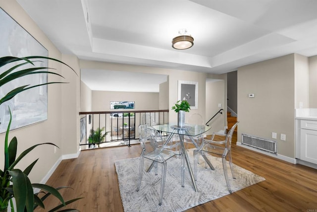 dining room with baseboards, visible vents, a tray ceiling, and wood finished floors