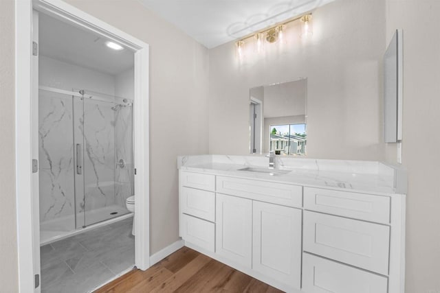 bathroom featuring a marble finish shower, baseboards, toilet, wood finished floors, and vanity