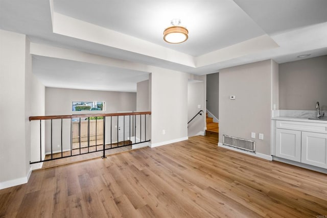 unfurnished room with a sink, visible vents, baseboards, a tray ceiling, and light wood finished floors