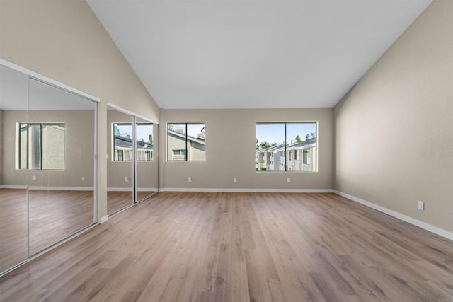 spare room featuring light wood-style floors, high vaulted ceiling, and baseboards