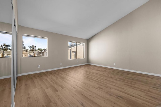 empty room featuring vaulted ceiling, light wood-style flooring, and baseboards