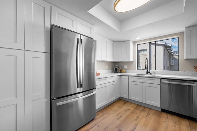 kitchen featuring appliances with stainless steel finishes, a raised ceiling, light countertops, and a sink