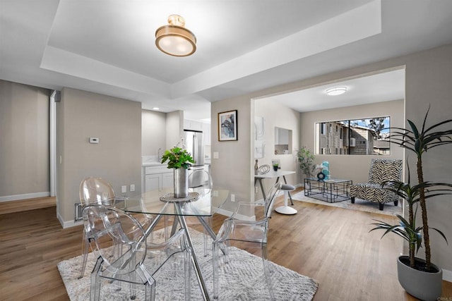 dining area featuring a tray ceiling, light wood-style flooring, and baseboards