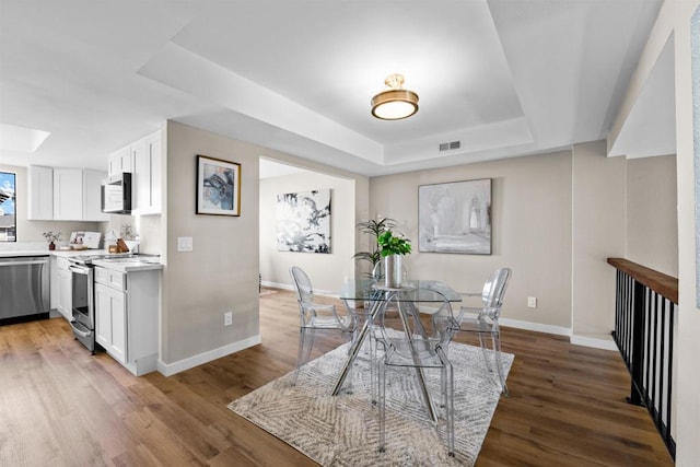 dining room featuring light wood-style floors, baseboards, visible vents, and a raised ceiling