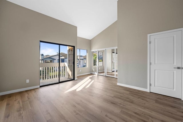 spare room with high vaulted ceiling, wood finished floors, and baseboards