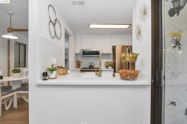 kitchen with hanging light fixtures, appliances with stainless steel finishes, sink, hardwood / wood-style flooring, and white cabinetry