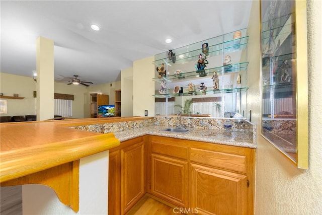 bar featuring light stone countertops, sink, ceiling fan, and light hardwood / wood-style flooring