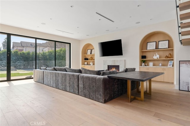 living room featuring a premium fireplace, built in features, and light hardwood / wood-style flooring