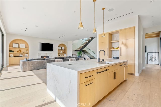 kitchen featuring a center island with sink, sink, light brown cabinets, and built in features