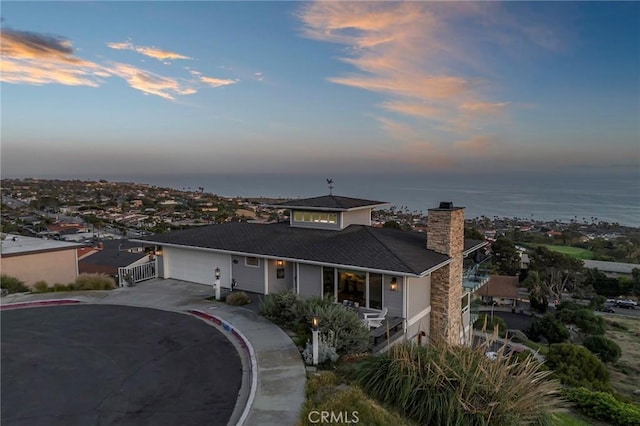 view of front of property with concrete driveway, a water view, a chimney, and a garage