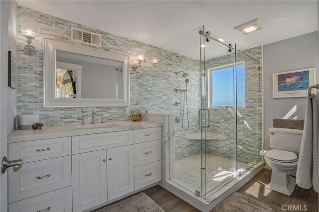 bathroom with toilet, an enclosed shower, vanity, hardwood / wood-style floors, and backsplash