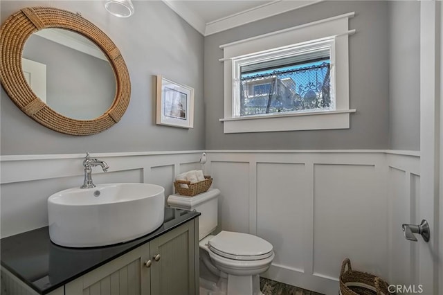 half bath with vanity, ornamental molding, a decorative wall, toilet, and a wainscoted wall
