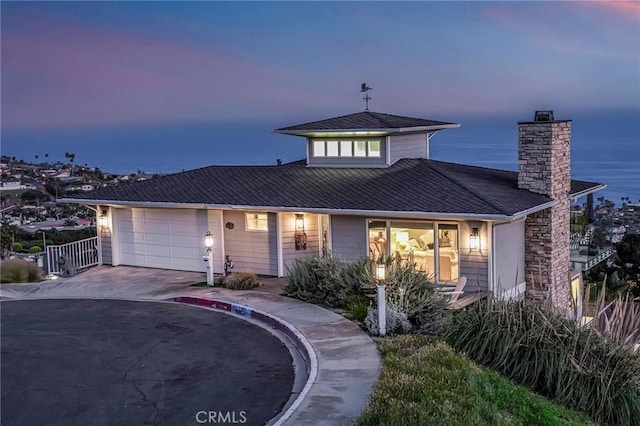 view of front of property featuring a water view, a chimney, an attached garage, and driveway