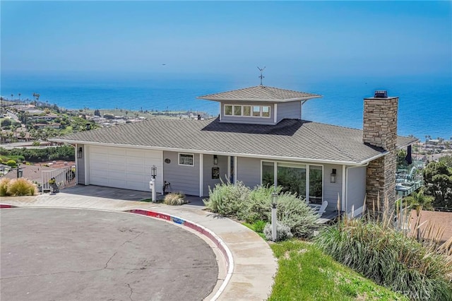 view of front of house with fence, a garage, a chimney, concrete driveway, and a water view
