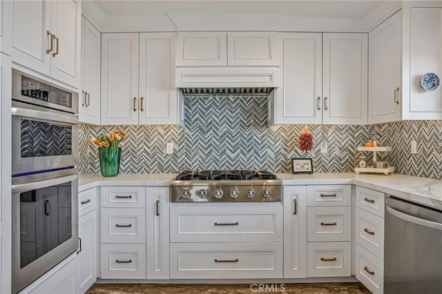 kitchen featuring stainless steel appliances, light stone countertops, white cabinets, and decorative backsplash