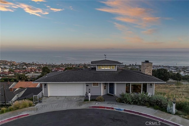 view of front of property with a water view, a chimney, an attached garage, and driveway