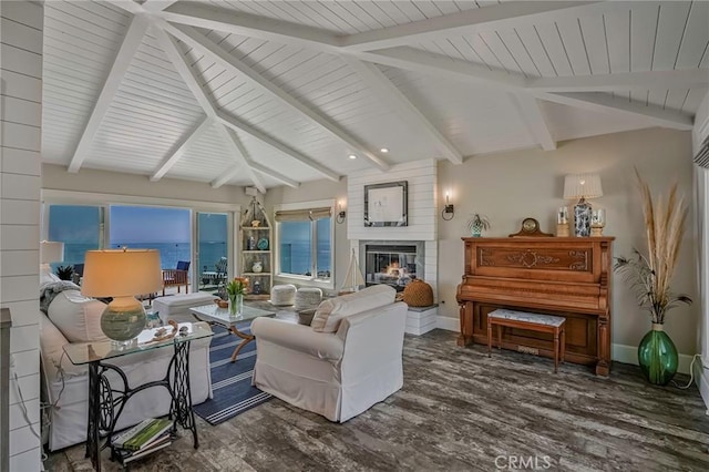 living area featuring baseboards, a glass covered fireplace, lofted ceiling with beams, and wood finished floors