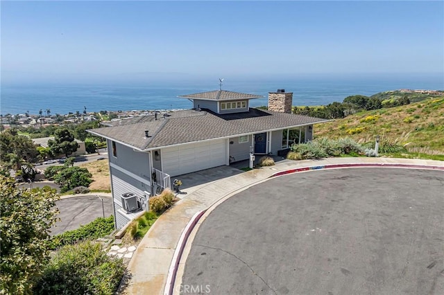 view of front of home featuring a chimney, a shingled roof, an attached garage, a water view, and driveway