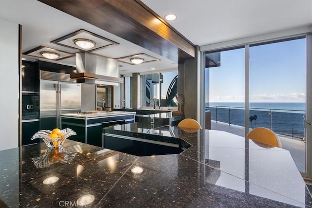 kitchen featuring a wall of windows, island range hood, a kitchen island, a water view, and dark stone countertops