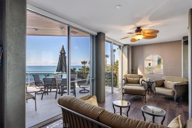 living room featuring wood-type flooring, a water view, a wall of windows, and ceiling fan