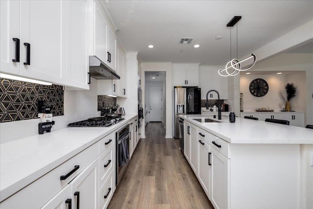 kitchen with pendant lighting, sink, white cabinets, tasteful backsplash, and an island with sink