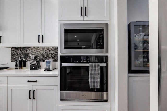 kitchen with stainless steel oven, tasteful backsplash, white cabinets, and built in microwave