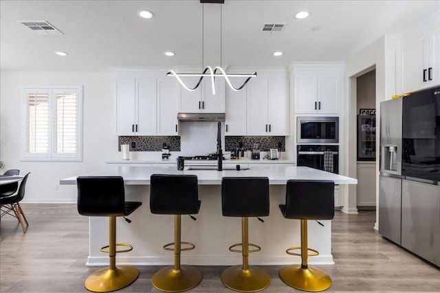 kitchen featuring decorative light fixtures, stainless steel refrigerator with ice dispenser, oven, a center island with sink, and built in microwave