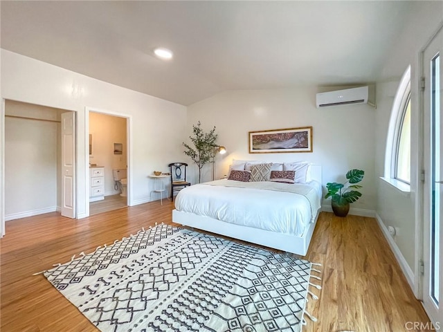 bedroom featuring light hardwood / wood-style floors, ensuite bathroom, a wall unit AC, and lofted ceiling