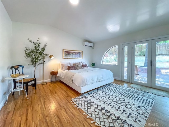 bedroom with an AC wall unit, wood-type flooring, french doors, access to exterior, and vaulted ceiling