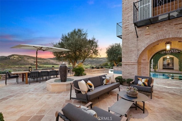 patio terrace at dusk featuring a balcony, an outdoor living space with a fireplace, and a mountain view