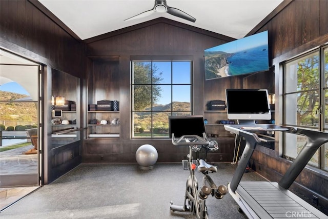 exercise area featuring ceiling fan, wooden walls, and vaulted ceiling