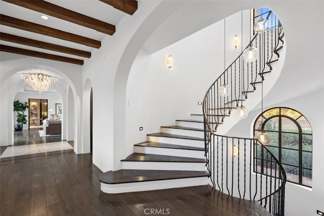 stairs with beamed ceiling, hardwood / wood-style floors, and a notable chandelier