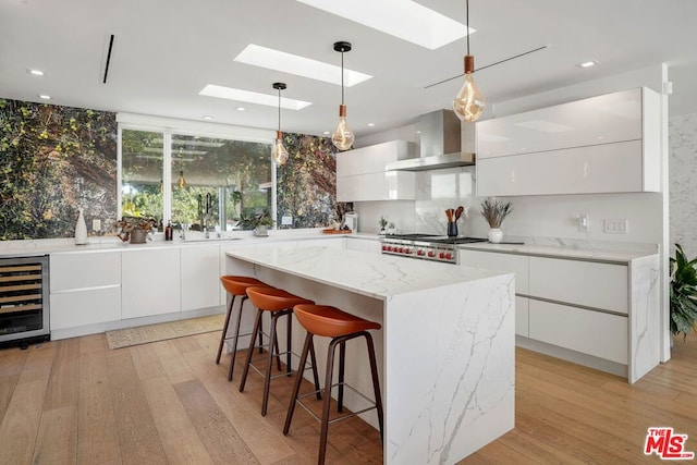 kitchen featuring wall chimney range hood, white cabinetry, a center island, and beverage cooler