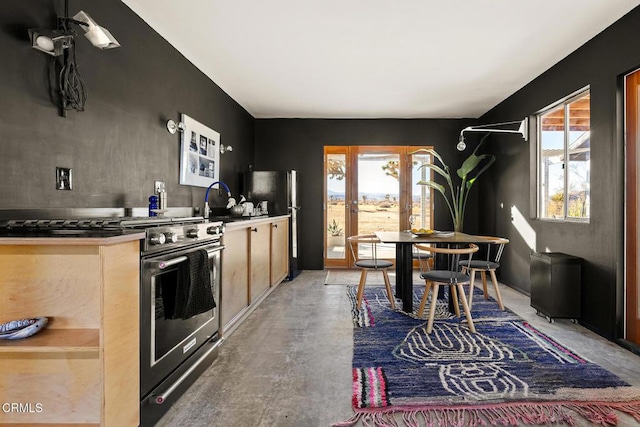 kitchen featuring concrete flooring, light brown cabinets, freestanding refrigerator, and high end stainless steel range oven