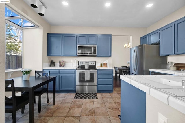 kitchen with blue cabinets, a chandelier, tile counters, light tile patterned floors, and stainless steel appliances